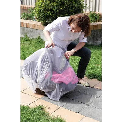A woman secures a Dreambaby Carrier Insect Netting over a colorful baby carrier on a patio, protecting it from insects.
