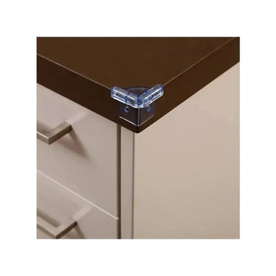 Clear corner cushion attached to the edge of a brown tabletop, designed for child safety.