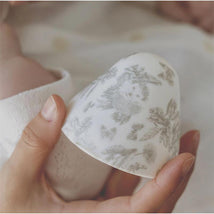 Baby bottle featuring floral designs, held by a caregiver, with a softly blurred baby in the background.