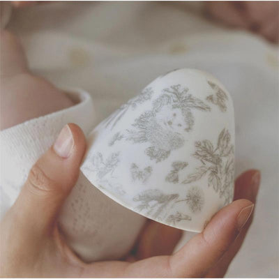 Baby bottle featuring floral designs, held by a caregiver, with a softly blurred baby in the background.