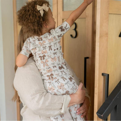 Toddler in a bow-patterned pajama set being held by an adult, reaching for storage with wooden lockers in the background.