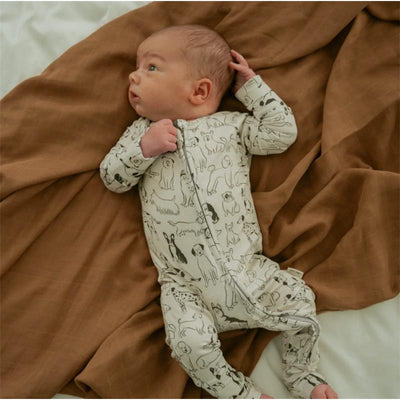 Baby wearing a cream-colored romper with a dog print, lying on a brown blanket, looking curiously to the side.