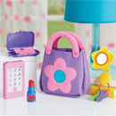 Toddler pretend play set featuring a purple purse with a pink flower, a toy phone, lipstick, and accessories including a mirror and keys.
