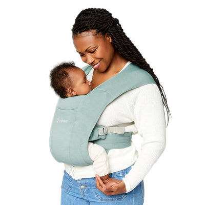 Ergobaby Embrace Newborn Baby Carrier in jade green, worn by a smiling woman, securely holding an infant.