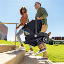 A man carries the Evenflo Shyft Dualride Infant Car Seat & Stroller Combo up steps, while a woman walks beside him, smiling.