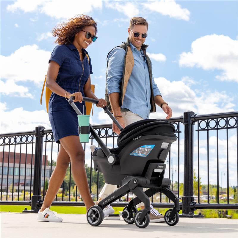 Couple walking outdoors, using the Evenflo Shyft Dualride Infant Car Seat & Stroller Combo in Beaufort Black.
