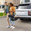 Couple walking together in a parking lot, carrying a baby in Evenflo Shyft Dualride Infant Car Seat, near a white vehicle.