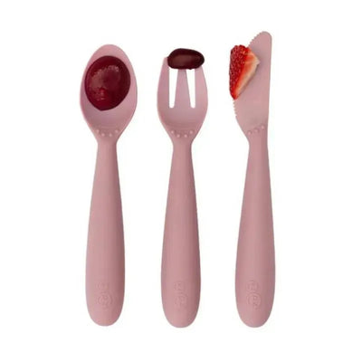 Set of three blush-colored utensils from Ezpz - Happy Utensils, including a spoon, fork, and knife, with food items shown.