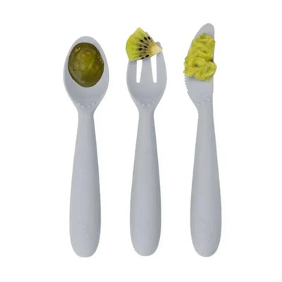 Set of three baby utensils in pewter color: spoon with green food, fork with kiwi, and knife with green spread.