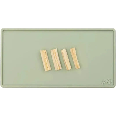Sage-colored Ezpz Tiny Placemat with four strips of food displayed on it.