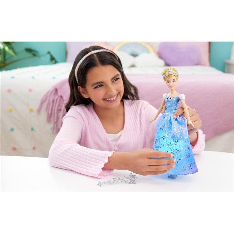 A child smiles while holding a Fisher Price Disney Princess Light Up Cinderella doll, featuring a blue dress and a magic wand.