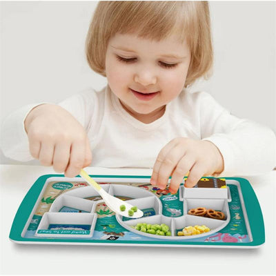 Child using a colorful Fred & Friends dinner tray, playfully placing peas into sections while smiling.