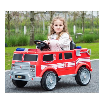 Child seated in a red Freddo fire truck toy, featuring emergency lights and number 911, on a pathway in a park.
