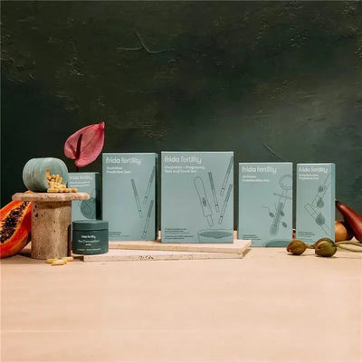 Frida Fertility ovulation prediction test strips displayed with other fertility products on a textured surface.