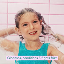 Child washing her hair with the Frida for Kids 2-in-1 Shampoo & Conditioner, displaying a happy expression and bubbles.