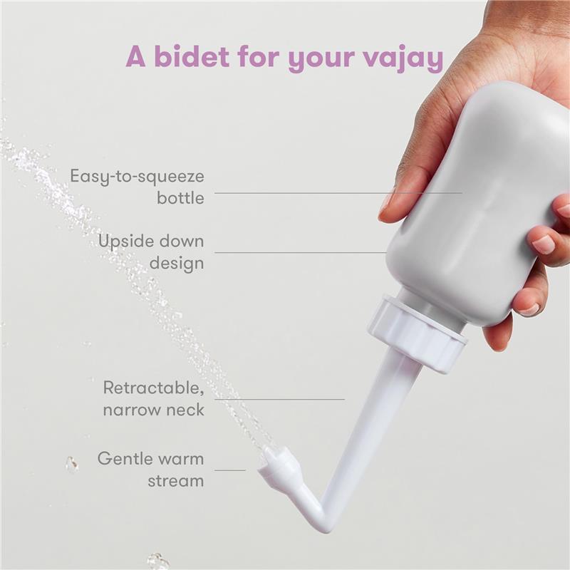 Gray Frida Mom Upside Down Peri Bottle sprayer held by a hand, demonstrating a gentle warm stream of water for postpartum care.