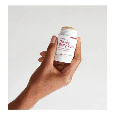 Fridababy Gassy Belly Rub in a hand, featuring a white container with pink text for tummy relief.