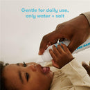 FridaBaby NoseFrida Saline Mist Spray being used on a child, who is laying down with a gentle hand applying the product.