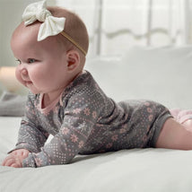 Baby girl wearing a gray long-sleeve onesie with a floral pattern, lying on her stomach on a soft surface.