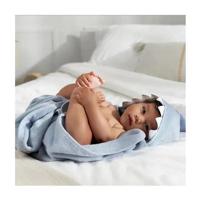 Baby wrapped in a light blue shark hooded towel on a bed, displaying cute expression and playful pose.