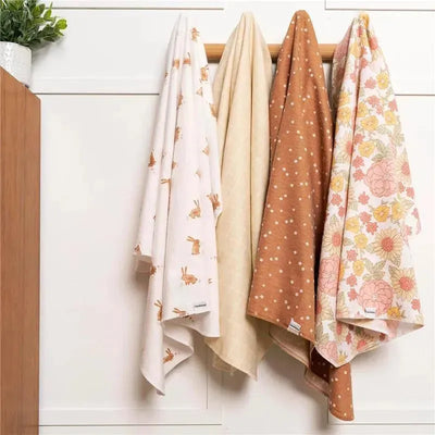 Four flannel baby blankets hanging on a wooden rod, featuring floral and animal prints in pastel colors.
