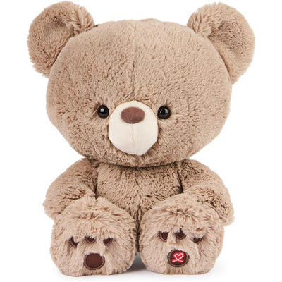 Soft, tan plush teddy bear with large eyes and stitched nose, featuring paw prints and heart logo on the foot.