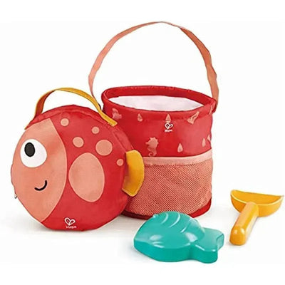 Fold and Go Beach Toy Set by Hape includes a fish-shaped bag, a red bucket, a teal shell mold, and a yellow shovel.