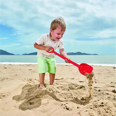 Child playing on the beach with a red Hape Mighty Sand Shovel, digging into the sand with excitement.