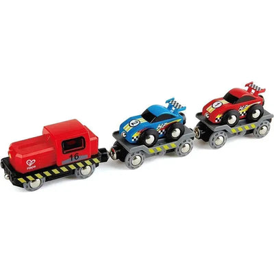 Red train engine pulling two toy race cars, one blue with a racing number, one red, both with checker patterns.