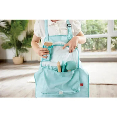 A child in a light blue apron uses a hair salon set, showing scissors, comb, and hairdryer inside a matching bag.