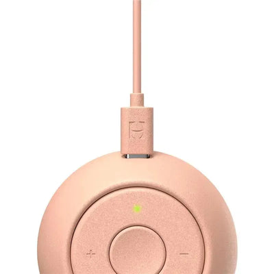 Hatch Rest Go portable sound machine in peach, featuring controls and a charging connection.