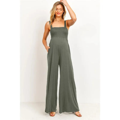 Sleeveless olive green smocked maternity wide-leg jumpsuit with pockets, worn by a smiling model.