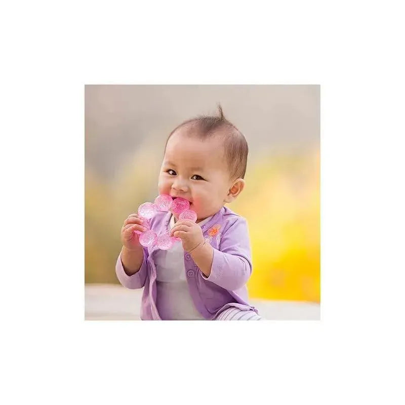 Baby smiling and holding a pink and lime water teether toy, dressed in a purple cardigan, against a blurred background.