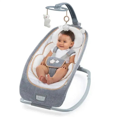 Infant seated in a grey rocking seat with a plush design, featuring hanging toys and a soft cushion for comfort.