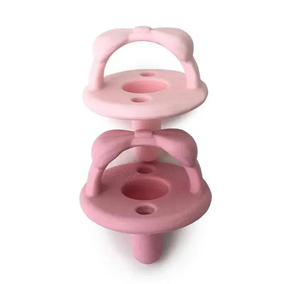 Two silicone pacifiers from Itzy Ritzy, featuring a bow design in light pink and dark pink colors.