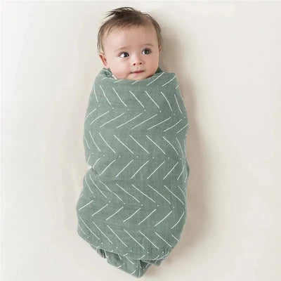 Multi-use breastfeeding cover in sage green, featuring a herringbone pattern, wrapping a baby with a curious expression.