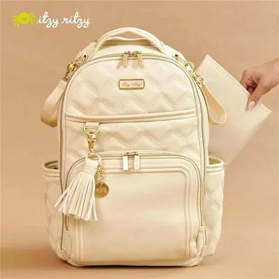 Large capacity Itzy Ritzy diaper bag backpack in cream, featuring quilted design and gold accents, with a changing pad being removed.