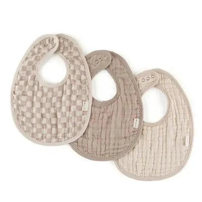 Three Itzy Ritzy Check Yes! bibs in soft, neutral colors, featuring textured patterns and adjustable snaps for easy wear.