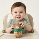 Smiling baby holding a bear-shaped snack container filled with cereal, seated at a high chair.