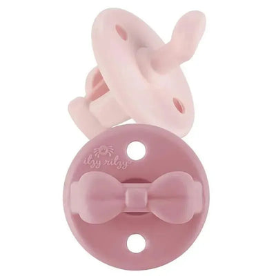 Orthodontic silicone pacifiers in ballet slipper and primrose colors, featuring a bow design, suitable for 0–6 months.