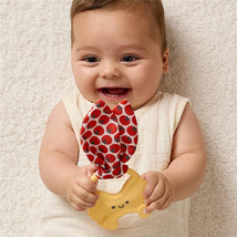 Baby smiling while holding an Itzy Ritzy Pasta Silicone Teether with a crinkle tie featuring a tomato pattern.
