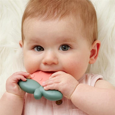 Infant holding a pink and green silicone strawberry-shaped teether with rattle sound, ready to chew.