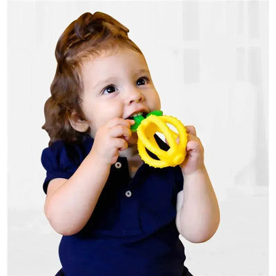 A toddler with curly hair smiles while holding and chewing a yellow silicone teething ball shaped like a lemon.