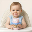 Baby sitting in a high chair, happily holding a pink kitty-themed snack cup filled with cereal rings.