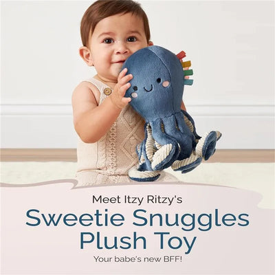Toddler hugs the Itzy Ritzy Sweetie Snuggles octopus plush toy, smiling while sitting on a light-colored floor.