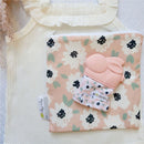 Teething mitt featuring a pink bunny design, placed on a floral-patterned pouch and a textured fabric backdrop.