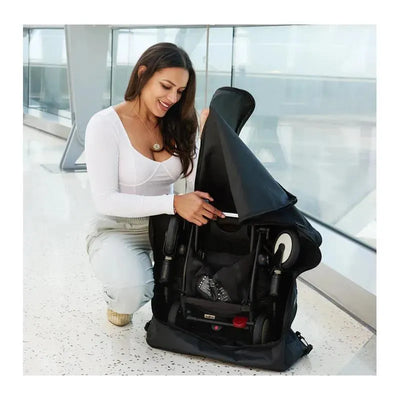 A woman is opening a padded black travel bag that holds a compact stroller, showcasing its protective features.