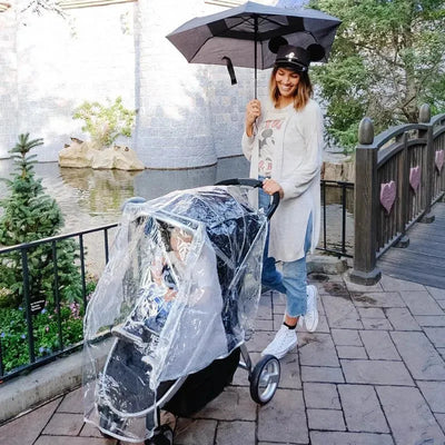 Universal stroller rain cover with a metallic Mickey design, protecting a child inside as a woman holds an umbrella.