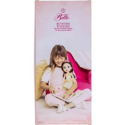A young girl sits on a pink couch holding a large Belle doll, smiling while reading a book.