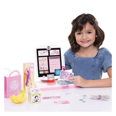Disney Princess-themed cash register playset with a girl holding play money, featuring various accessories like bags and fruit.